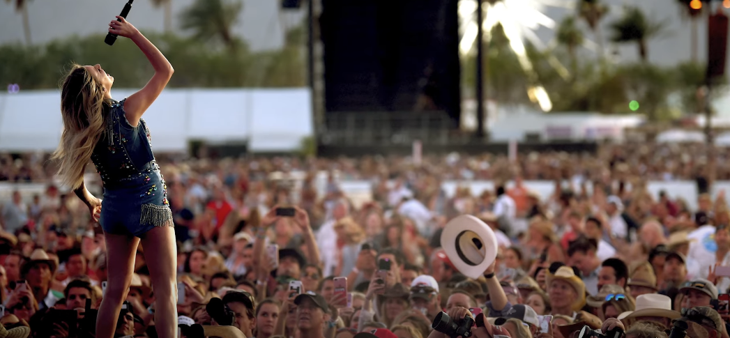 Photo of a girl singing on stage, with a large crowd of people watching her concert