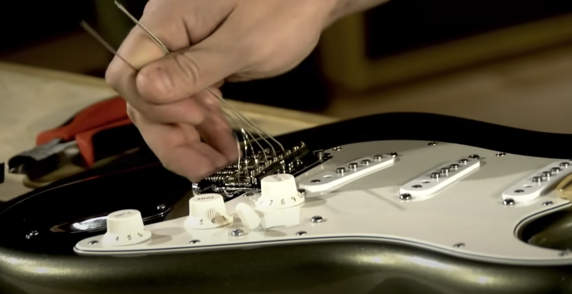 Photo of a hand removing strings from a guitar