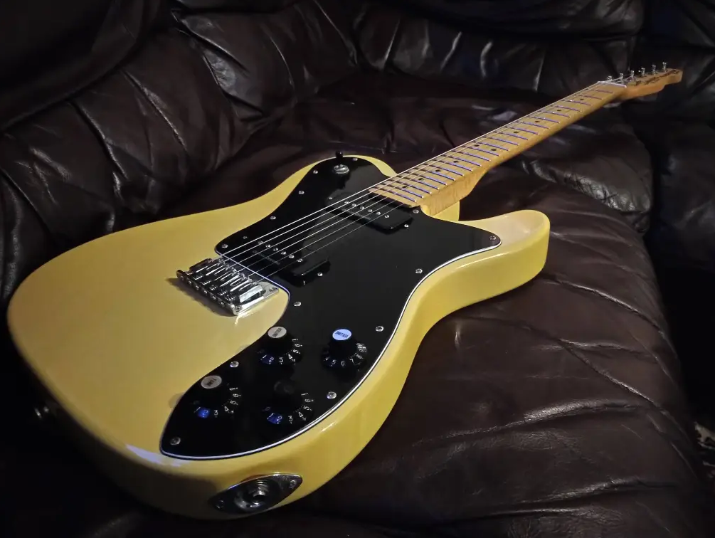 Side view of a Squier Telecaster Custom electric guitar on black leather sofa