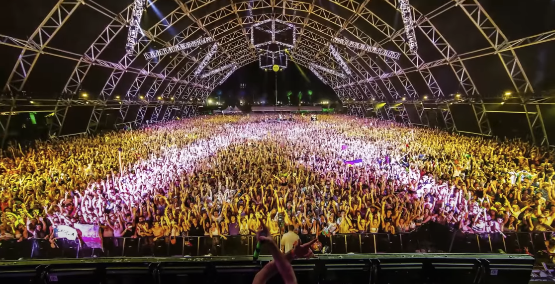 Photo of a massive crowd at a nighttime concert, with vibrant lights creating a striking contrast against the darkness