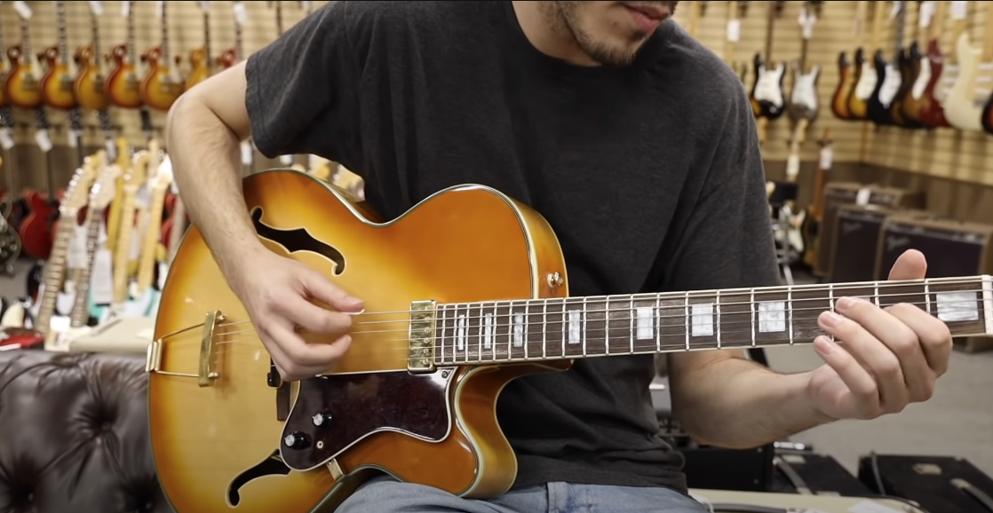 Photo of a guy playing a guitar with multiple guitars in the background